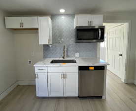 Kitchen featuring white cabinetry, stainless steel appliances, tasteful backsplash, light wood finished floors, and light stone counters
