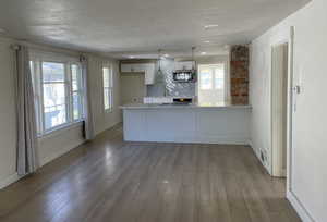 Kitchen featuring a peninsula, pendant lighting, tasteful backsplash, white cabinetry, and light wood-style floors