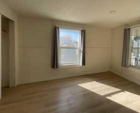 Unfurnished bedroom with multiple windows, light wood finished floors, and a textured ceiling
