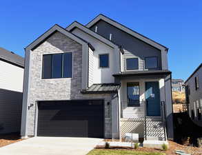 View of front of house with stone siding, an attached garage, driveway, and a standing seam roof