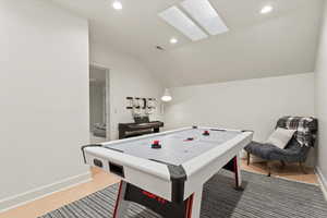 Rec room featuring a skylight, vaulted ceiling, light wood finished floors, and recessed lighting