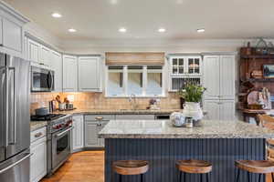 Kitchen with a breakfast bar area, high quality appliances, gray cabinets, ornamental molding, and light stone counters