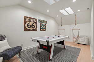 Recreation room with vaulted ceiling, recessed lighting, a skylight, and light wood-style floors