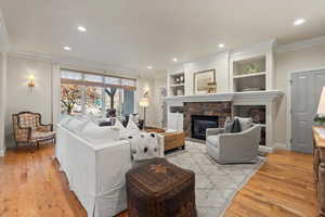 Living area featuring a stone fireplace, ornamental molding, recessed lighting, built in shelves, and light wood-type flooring