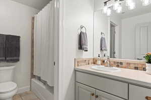 Full bathroom featuring light tile patterned flooring, vanity, shower / bathtub combination with curtain, and backsplash