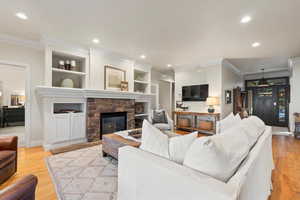 Living room featuring crown molding, light wood-type flooring, a stone fireplace, recessed lighting, and built in features