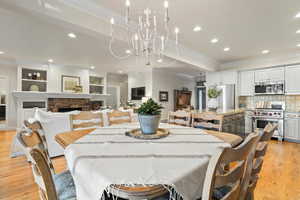 Dining space with light wood finished floors, ornamental molding, a fireplace, recessed lighting, and a chandelier