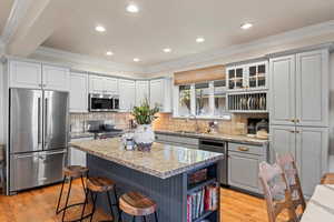 Kitchen featuring open shelves, appliances with stainless steel finishes, ornamental molding, gray cabinets, and light wood-style floors
