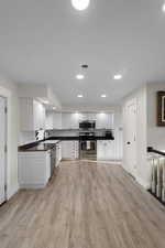 Kitchen with white cabinets, recessed lighting, light wood-style flooring, dark countertops, and stainless steel appliances