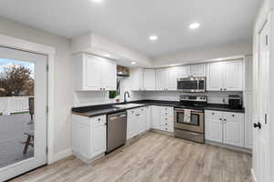 Kitchen featuring stainless steel appliances, dark countertops, white cabinets, plenty of natural light, and recessed lighting