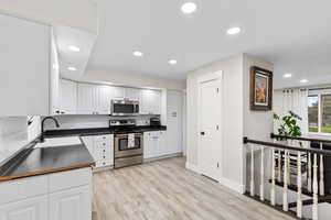 Kitchen with dark countertops, appliances with stainless steel finishes, white cabinetry, recessed lighting, and light wood finished floors