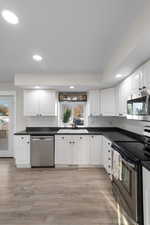 Kitchen featuring white cabinets, dark countertops, appliances with stainless steel finishes, and recessed lighting