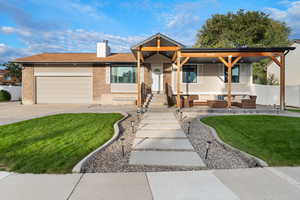View of front of home featuring an attached garage, a chimney, brick siding, concrete driveway, and covered porch