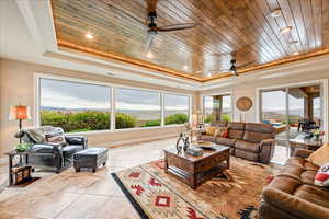 Living area featuring a tray ceiling, wood ceiling, light tile patterned floors, a mountain view, and ceiling fan