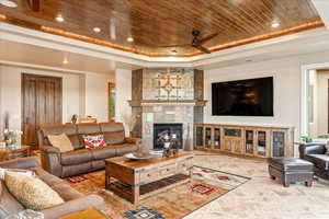 Living area with wood ceiling, a raised ceiling, a ceiling fan, a tiled fireplace, and recessed lighting