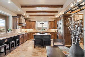 Kitchen with a breakfast bar, decorative light fixtures, a kitchen island, backsplash, and light stone countertops
