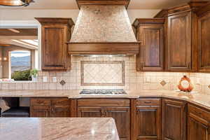 Kitchen with custom exhaust hood, tasteful backsplash, light stone countertops, and stainless steel gas cooktop