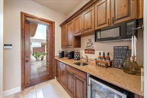 Kitchenet with light stone countertops, beverage cooler, black microwave, light tile patterned floors, and brown cabinets