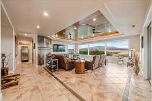 Living room featuring a tray ceiling, inlaid floor details, light tile patterned floors, a ceiling fan, and recessed lighting