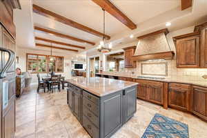 Kitchen featuring hanging light fixtures, decorative backsplash, light stone counters, beam ceiling, and a center island