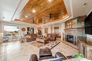 Tiled living area featuring a tray ceiling, wooden ceiling, a fireplace, crown molding, and recessed lighting
