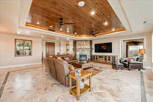 Living room with a raised ceiling, wooden ceiling, recessed lighting, a tiled fireplace, and a ceiling fan