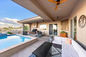 Fenced backyard with a ceiling fan, a patio area, outdoor lounge area, an outdoor kitchen, and a pool with connected hot tub