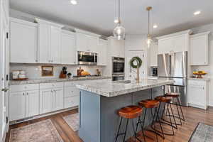 Kitchen with tasteful backsplash, stainless steel appliances, dark wood-style floors, light stone countertops, and recessed lighting