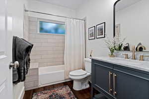Full bath with vanity, shower / tub combo with curtain, and dark wood-style flooring