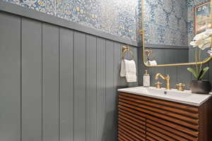 Bathroom featuring vanity, wallpapered walls, and a wainscoted wall