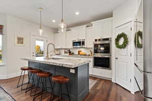 Kitchen with decorative backsplash, white cabinets, appliances with stainless steel finishes, decorative light fixtures, and light stone counters