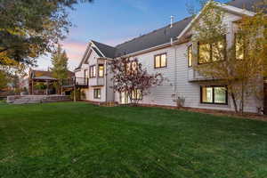 Back of property at dusk with a lawn, a gazebo, and a shingled roof