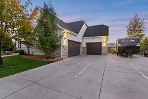 View of side of property with driveway, an attached garage, a shingled roof, a yard, and stone siding