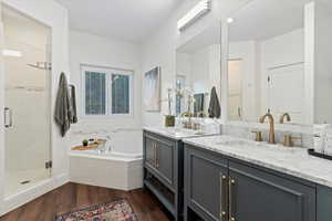 Full bath with dark wood-style floors, two vanities, a bath, and a shower stall