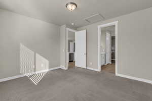 Unfurnished bedroom featuring carpet flooring, attic access, and ensuite bathroom