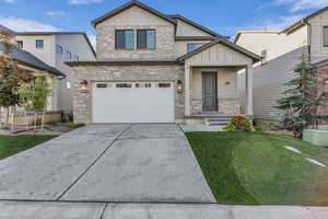 View of front facade with board and batten siding, driveway, brick siding, an attached garage, and a front yard
