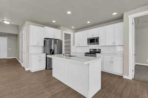 Kitchen featuring backsplash, white cabinets, appliances with stainless steel finishes, a kitchen island with sink, and recessed lighting