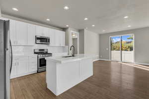 Kitchen with stainless steel appliances, white cabinetry, recessed lighting, decorative backsplash, and an island with sink