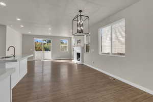 Unfurnished living room featuring a fireplace with raised hearth, recessed lighting, dark wood-style floors, and a chandelier