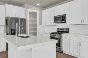 Kitchen with backsplash, stainless steel appliances, a center island with sink, white cabinets, and recessed lighting