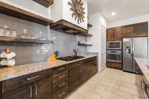 Kitchen with open shelves, dark brown cabinetry, tasteful backsplash, stainless steel appliances, and light stone counters