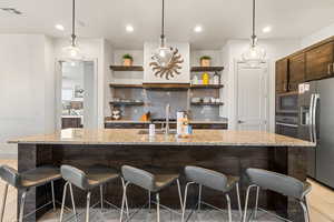 Kitchen with pendant lighting, tasteful backsplash, a kitchen bar, stainless steel appliances, and dark brown cabinets
