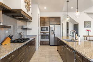 Kitchen featuring tasteful backsplash, stainless steel appliances, light stone counters, hanging light fixtures, and dark brown cabinets