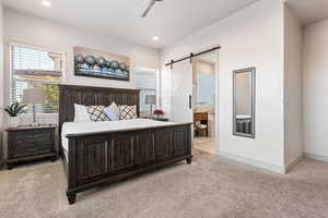 Bedroom with a barn door, light colored carpet, multiple windows, ensuite bath, and recessed lighting