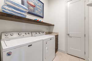 Washroom with washing machine and dryer and light tile patterned flooring