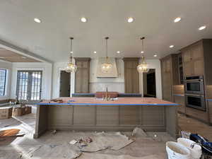 Kitchen with a large island with sink, stainless steel double oven, a breakfast bar, french doors, and hanging light fixtures