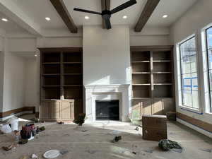 Unfurnished living room featuring beam ceiling, a fireplace, ceiling fan, and build-in cabinets.