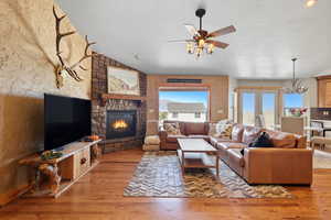 Living area with lofted ceiling, a textured ceiling, light wood-style flooring, a fireplace, and ceiling fan