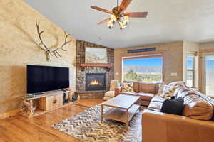Living room with lofted ceiling, a textured ceiling, wood finished floors, a textured wall, and a fireplace