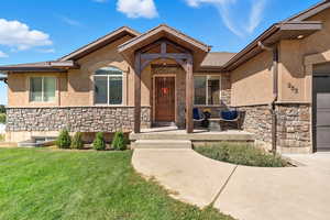 Doorway to property featuring stone siding, stucco siding, a yard, and covered porch